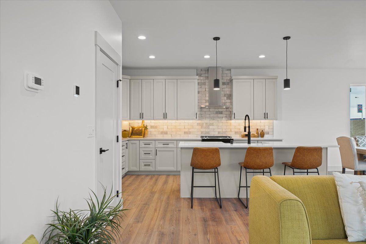Bright modern kitchen with white cabinets, marble island, wood floors, and tan bar stools in an open living space