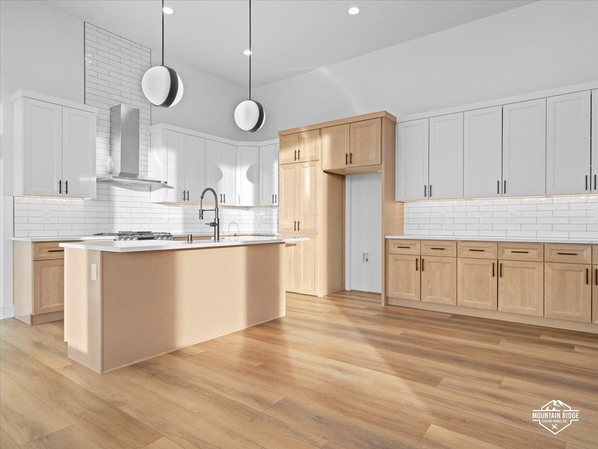 Bright modern kitchen with light wood floors, white cabinets, and a central island with pendant lights