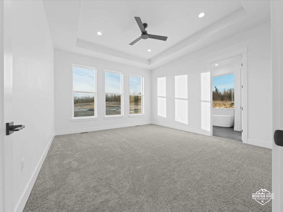 Bright empty bedroom with gray carpet, white walls, large windows, and a ceiling fan