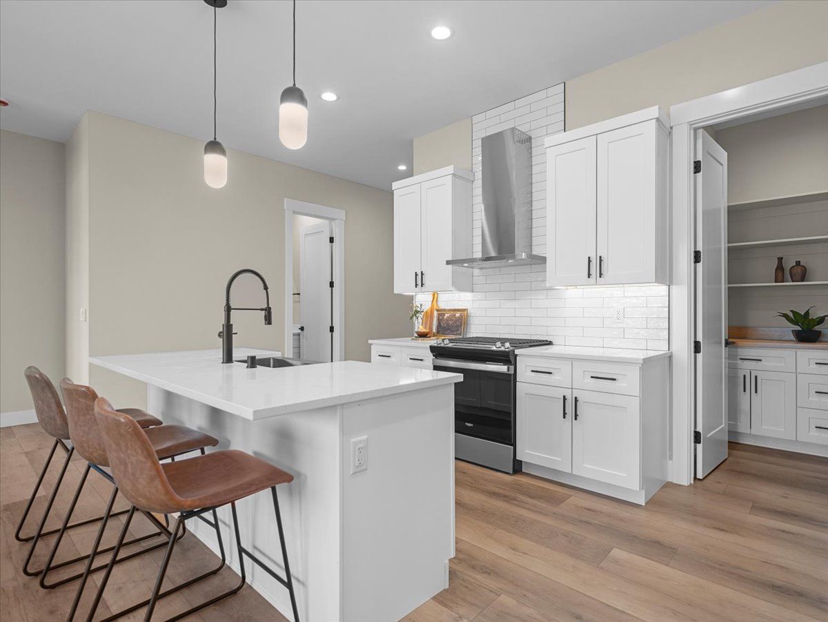 Modern white kitchen with island, pendant lights, wood flooring, and barstools