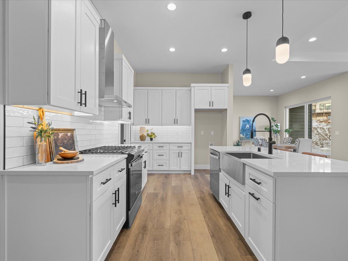 Bright modern white kitchen with wood floors, island sink, and stainless steel appliances