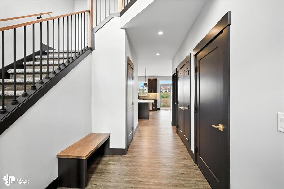 Modern hallway with dark doors, staircase, wood floor, and kitchen visible at the end