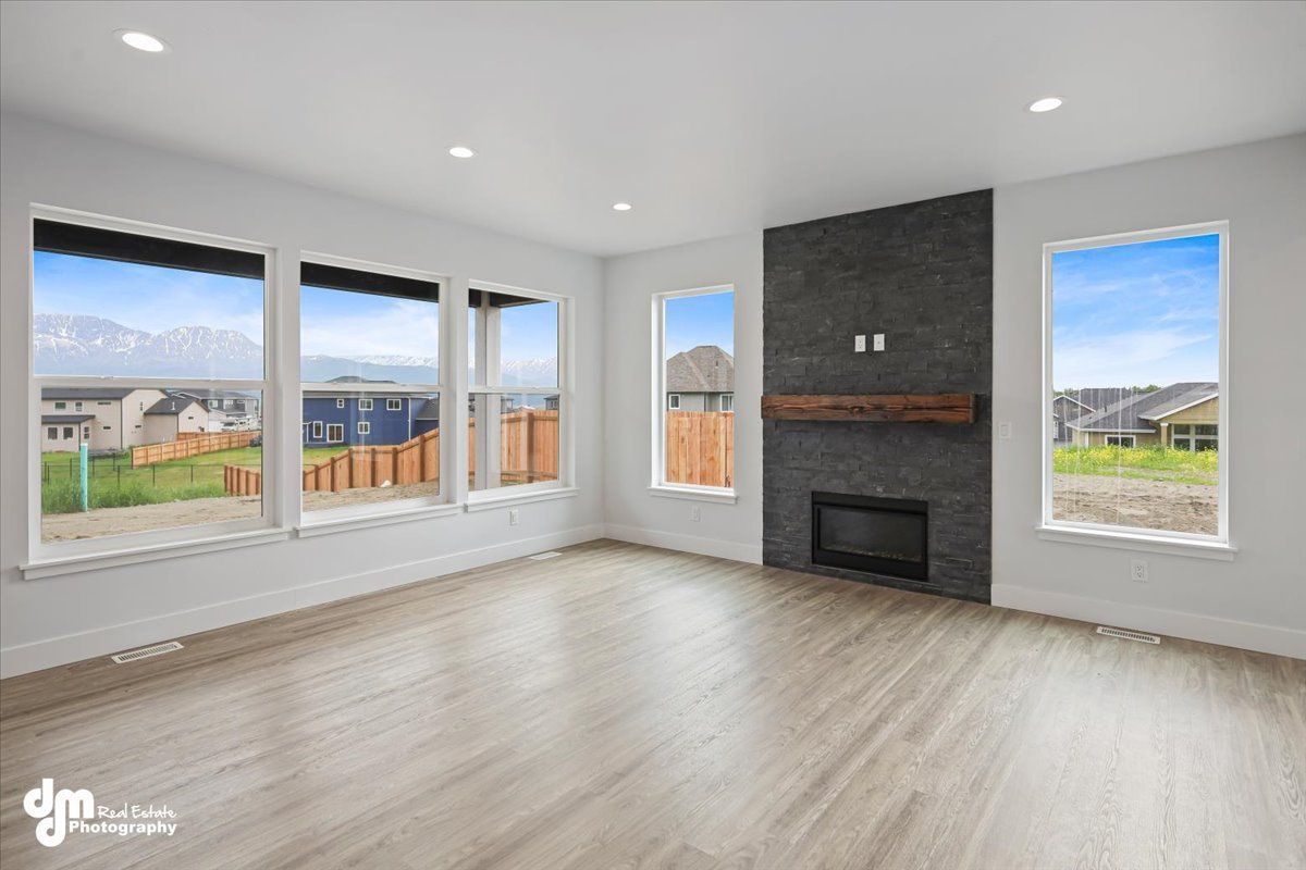Bright empty living room with large windows, gray fireplace wall, and light wood floors