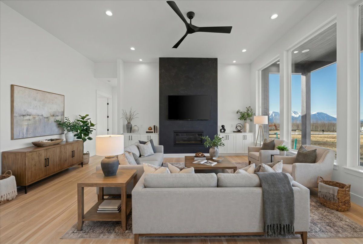 Modern living room with light wood floors, gray sectional, fireplace, and large windows overlooking mountains
