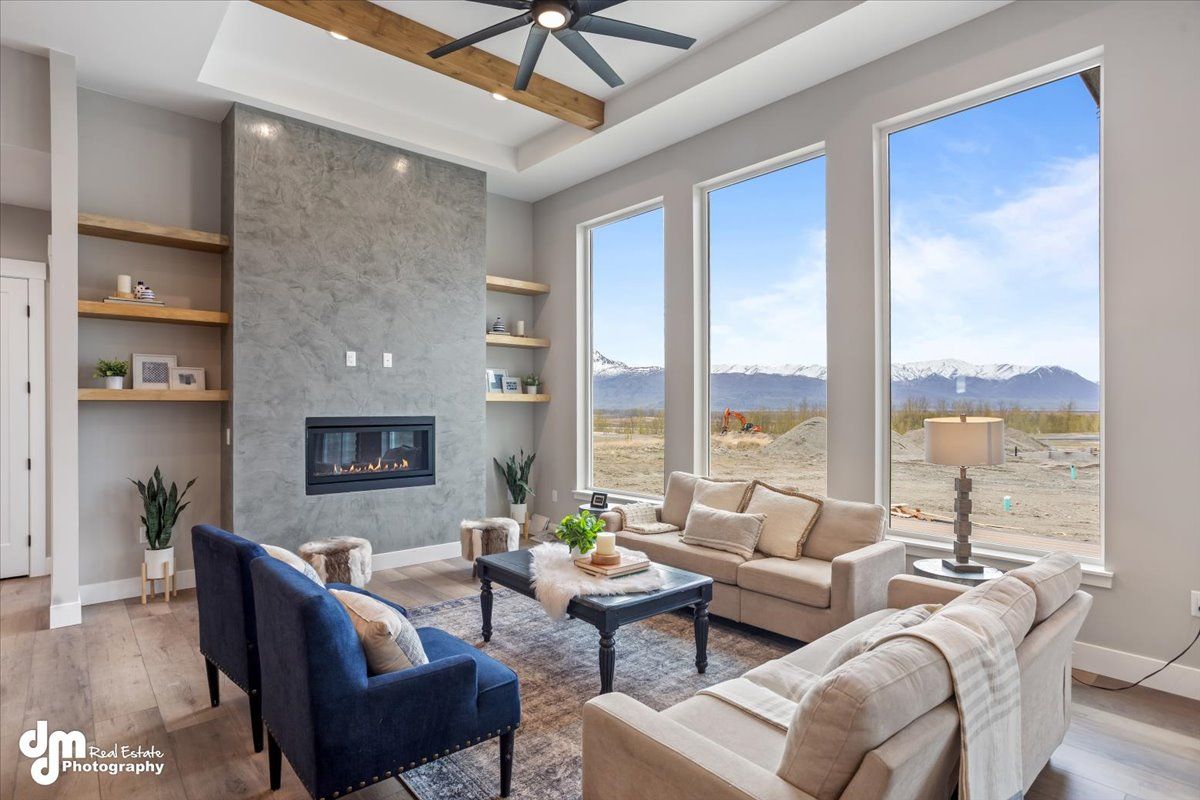 Bright living room with fireplace, beige and blue sofas, and large windows overlooking mountains and sky