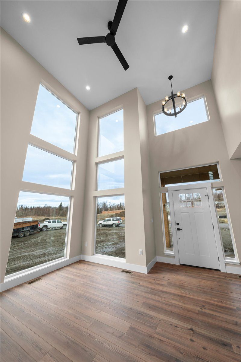 Bright empty room with tall windows, wood floor, black ceiling fan, and white front door