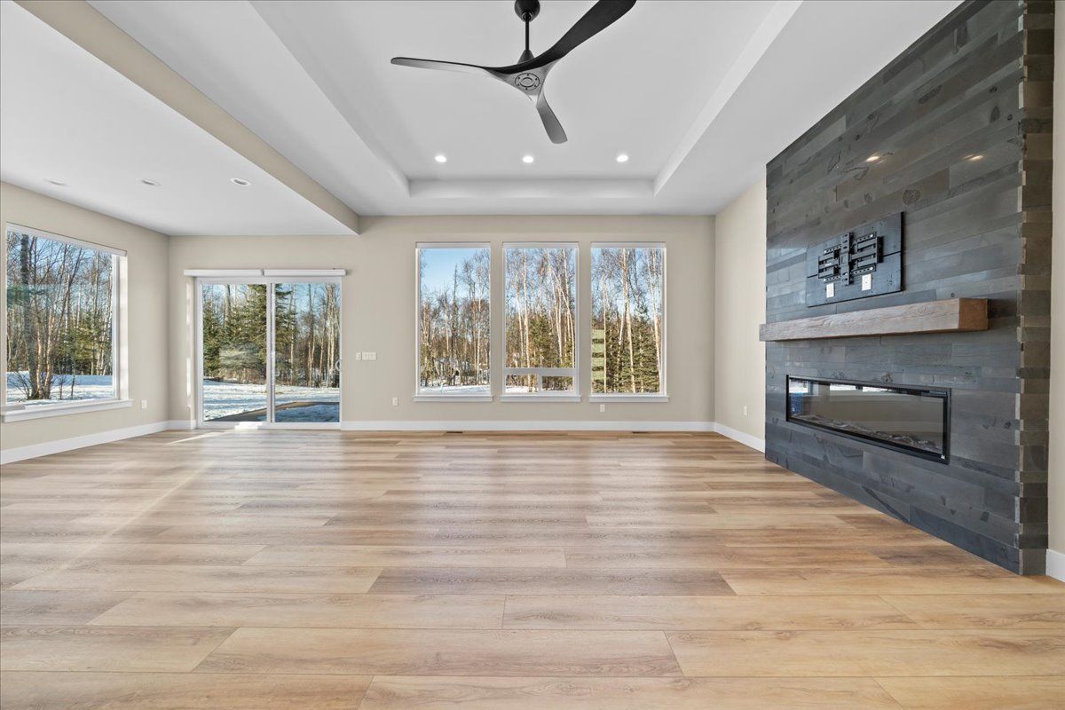 Spacious modern living room with hardwood floors, large windows, a ceiling fan, and a stone fireplace