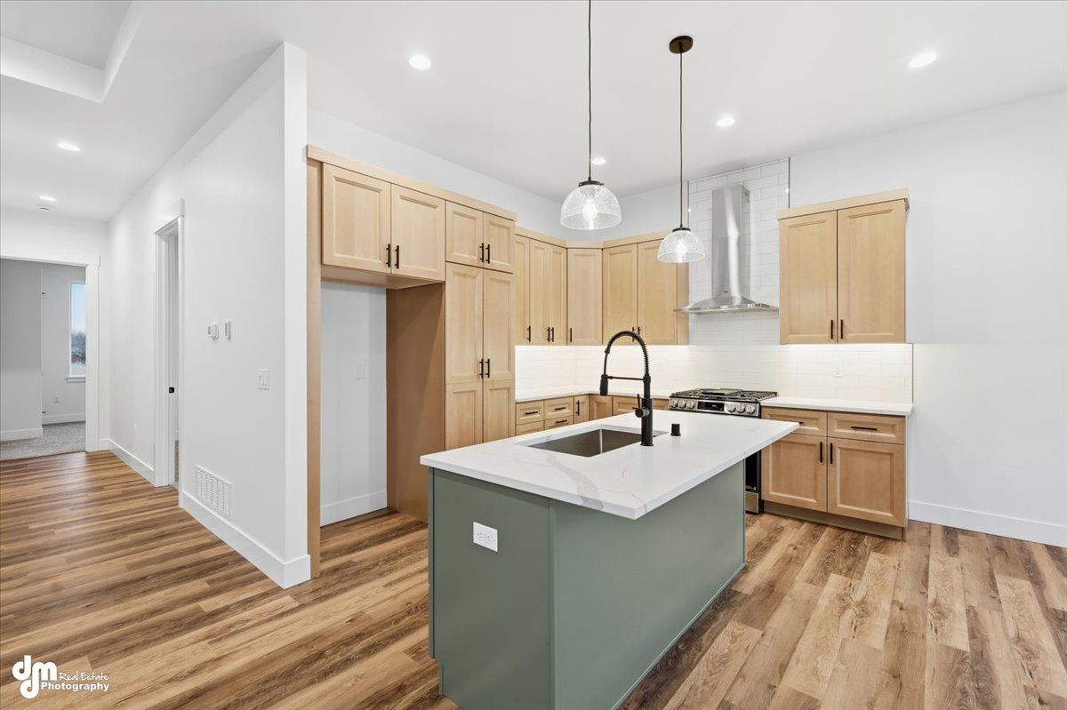 Bright modern kitchen with white cabinets, wood floors, and a gray island with sink and pendant lights
