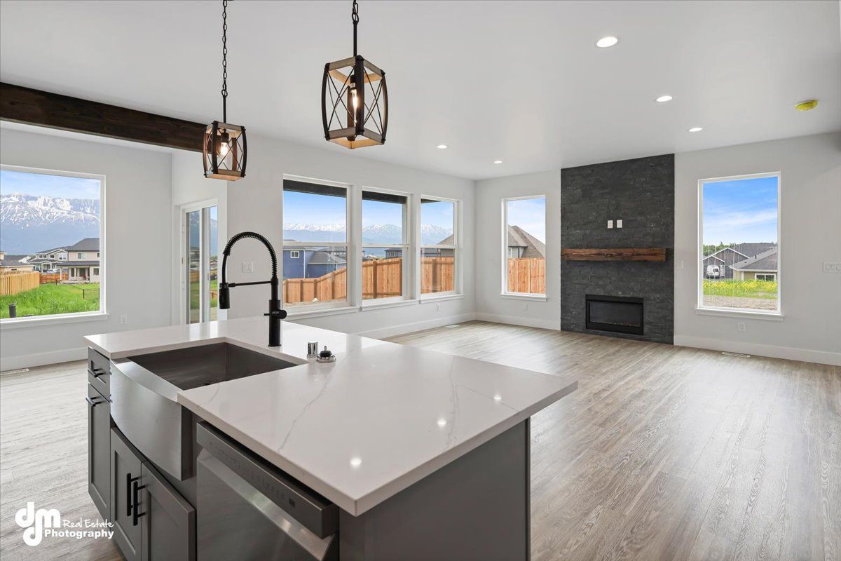 Modern open-plan kitchen and living room with large windows, island sink, and fireplace.
