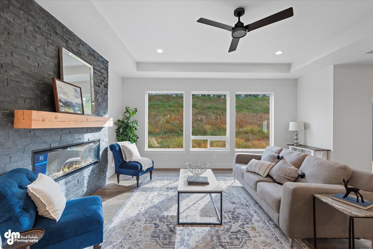 Modern living room with gray sofa, blue chair, fireplace, and large windows overlooking greenery