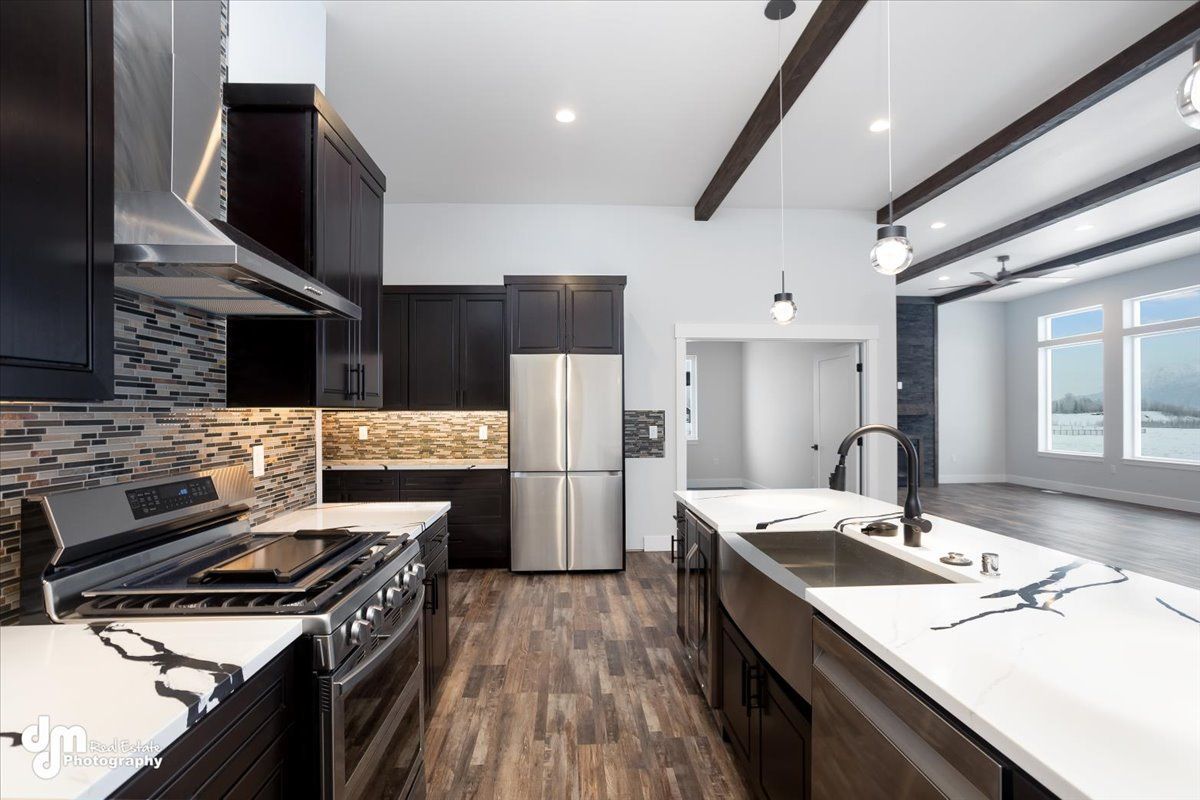 Modern kitchen with dark cabinets, white island countertops, stainless steel appliances, and wood floors