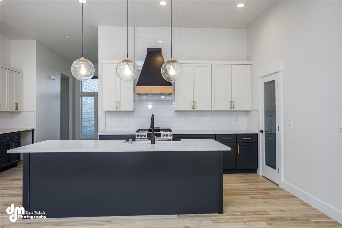 Modern kitchen with white cabinets, navy island, black hood, and wood floors