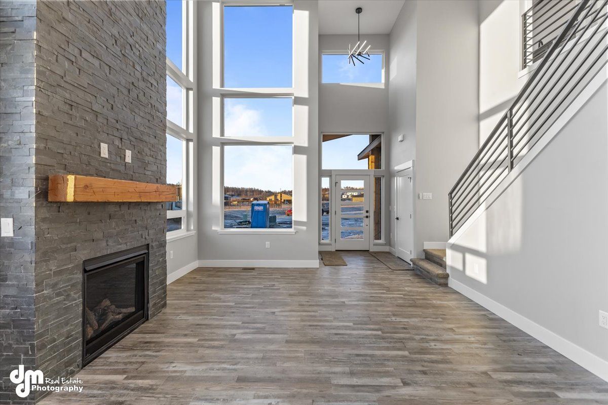 Modern living room with tall windows, stone fireplace, wood floors, and staircase railing