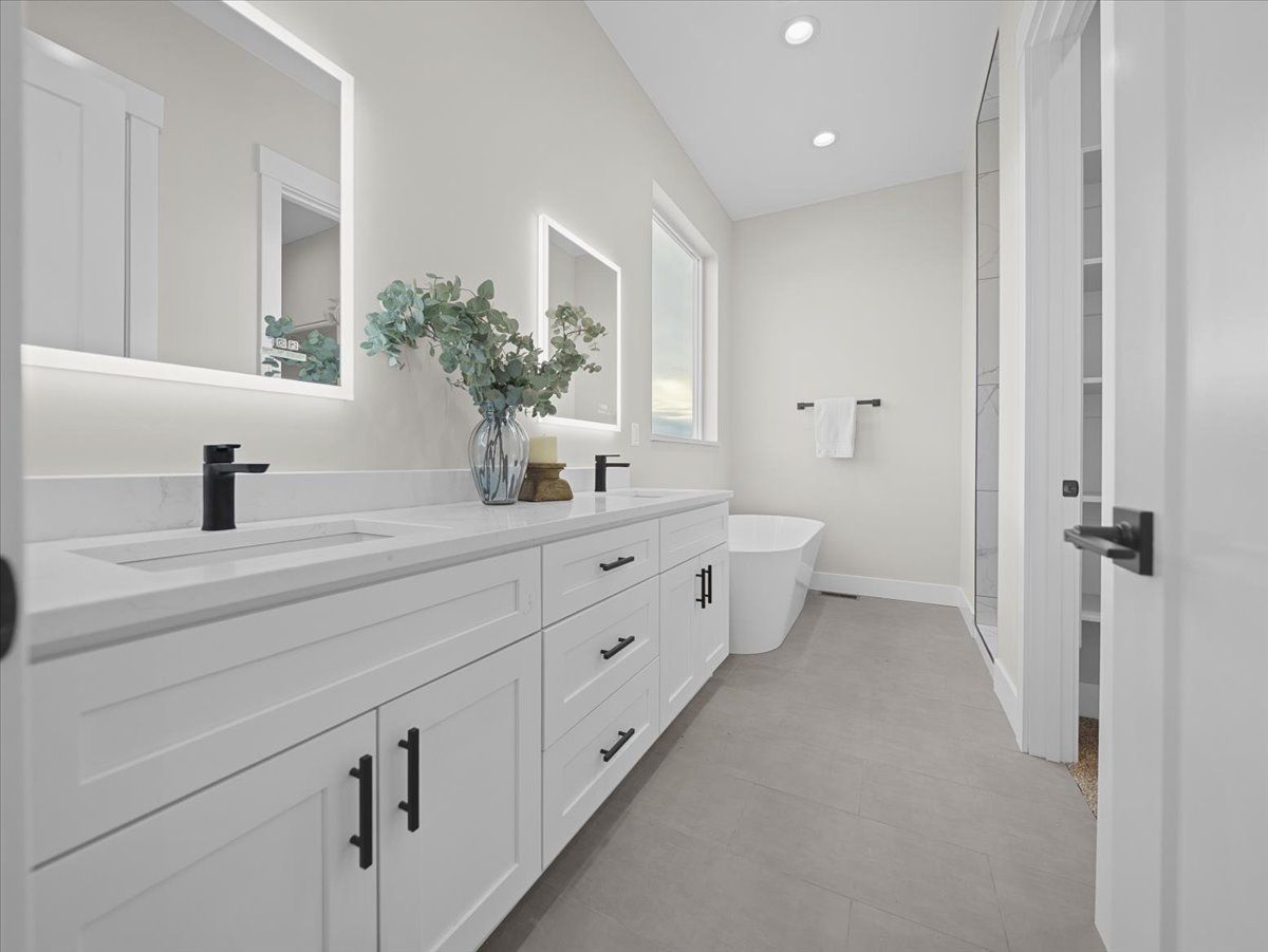 Bright modern bathroom with white vanity, mirrors, bathtub, and light gray floor
