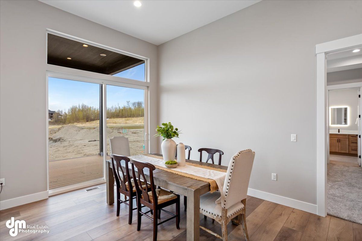 Bright dining area with wooden table, chairs, and large sliding glass doors overlooking a sandy yard.