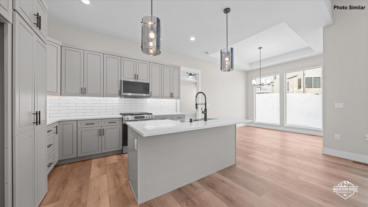 Bright modern kitchen with gray cabinets, white island, pendant lights, and hardwood floors