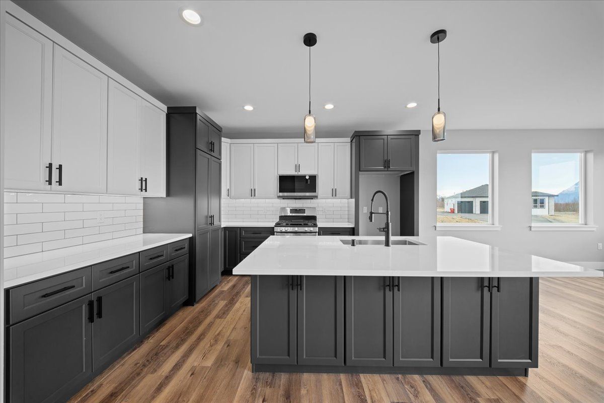 Modern kitchen with dark lower cabinets, white island, wood floors, and pendant lights