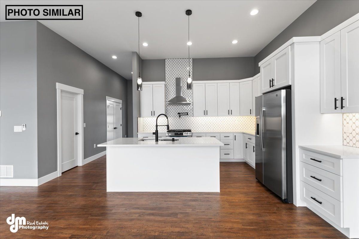 Modern white kitchen with island, stainless steel appliances, pendant lights, and hardwood floors