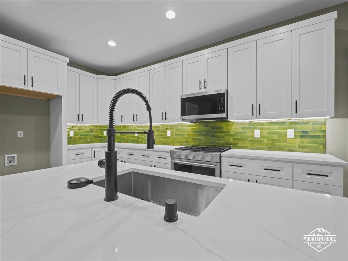Modern white kitchen with marble island, black faucet, stainless appliances, and green tile backsplash
