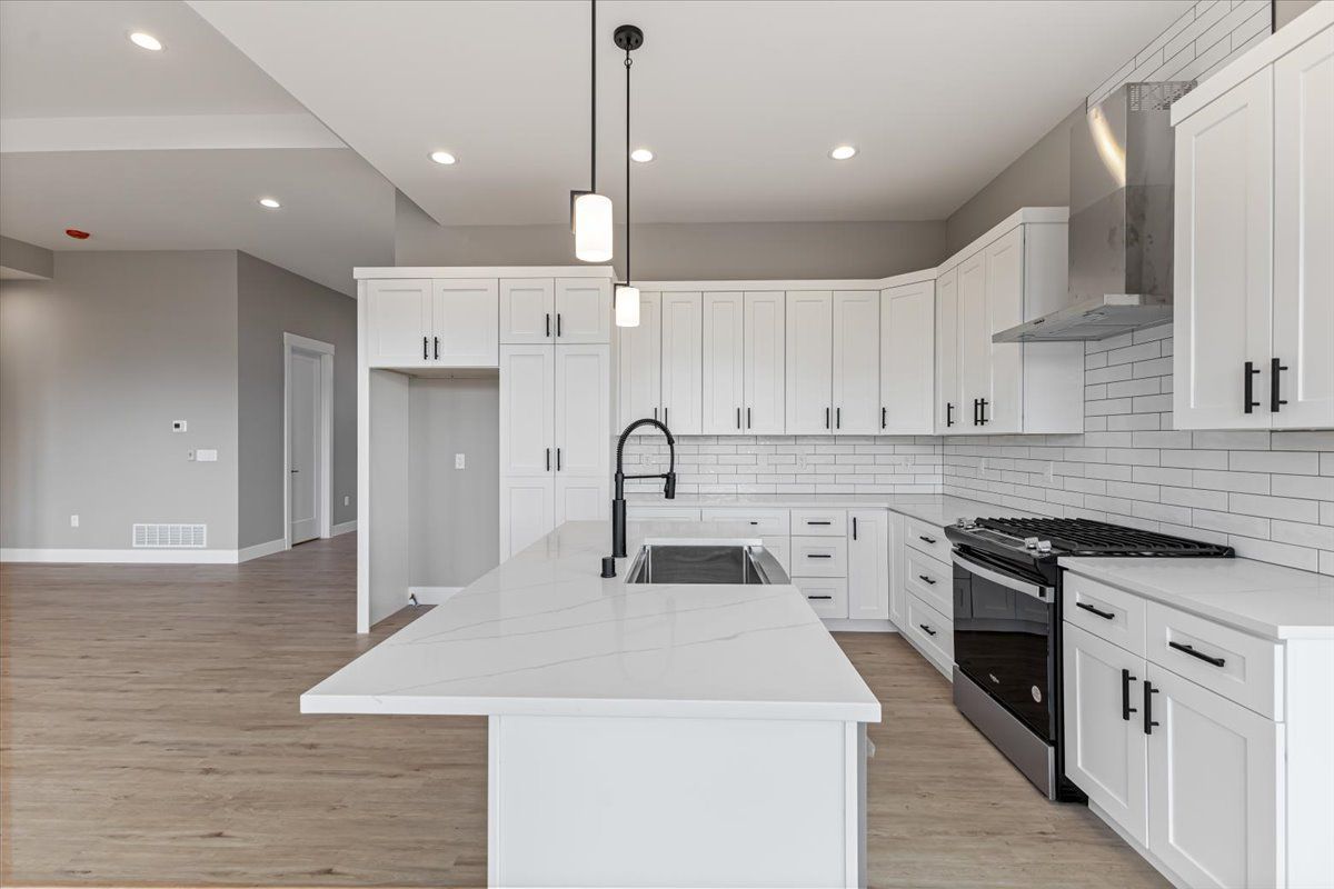 Bright, modern white kitchen with island, pendant lights, and stainless steel appliances