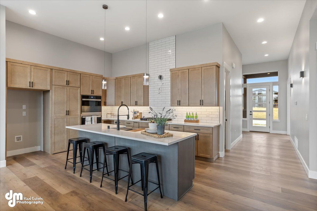 Modern kitchen with large island, wood cabinets, bar stools, and bright open layout leading to a hallway