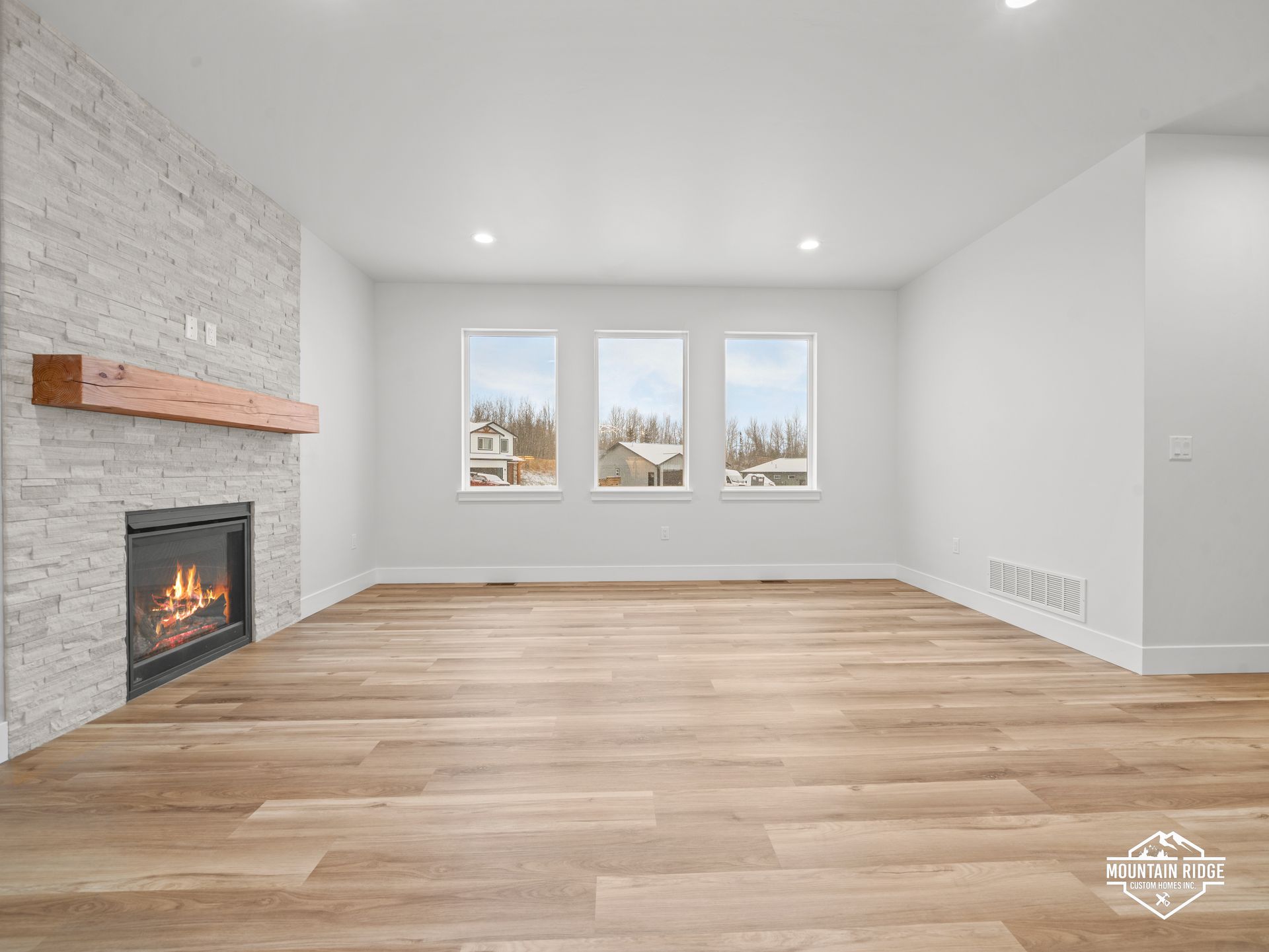 Empty modern living room with white walls, wood floors, fireplace, and three windows