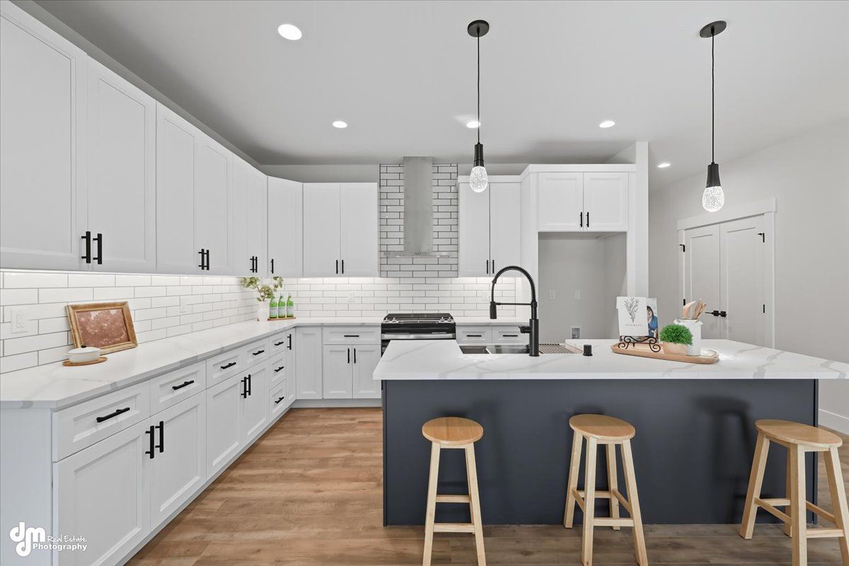Bright modern kitchen with white cabinets, wood floors, gray island, and two stools
