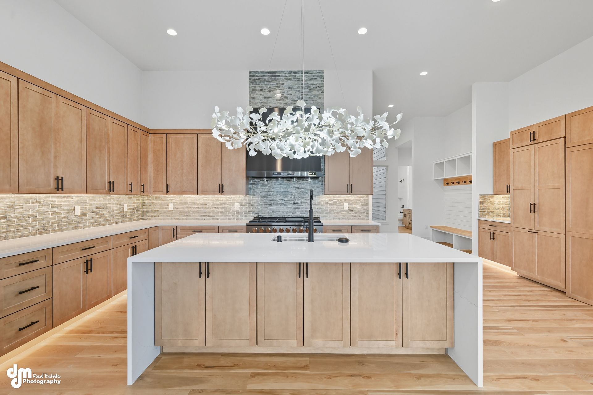 Bright modern kitchen with wood cabinets, white island, marble backsplash, and chandelier-lit ceiling