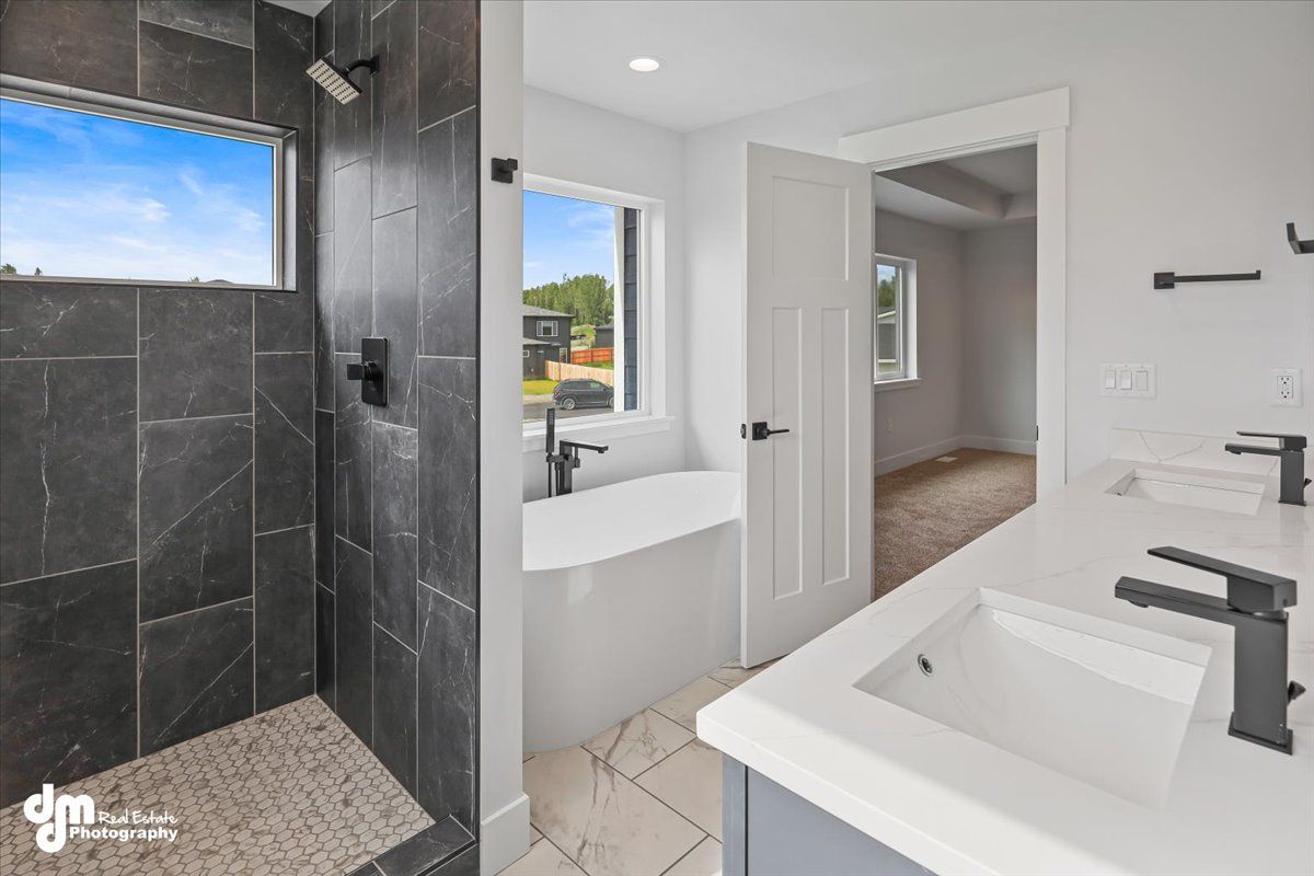 Modern bathroom with walk-in black tile shower, double sinks, and open doorway to a bedroom.