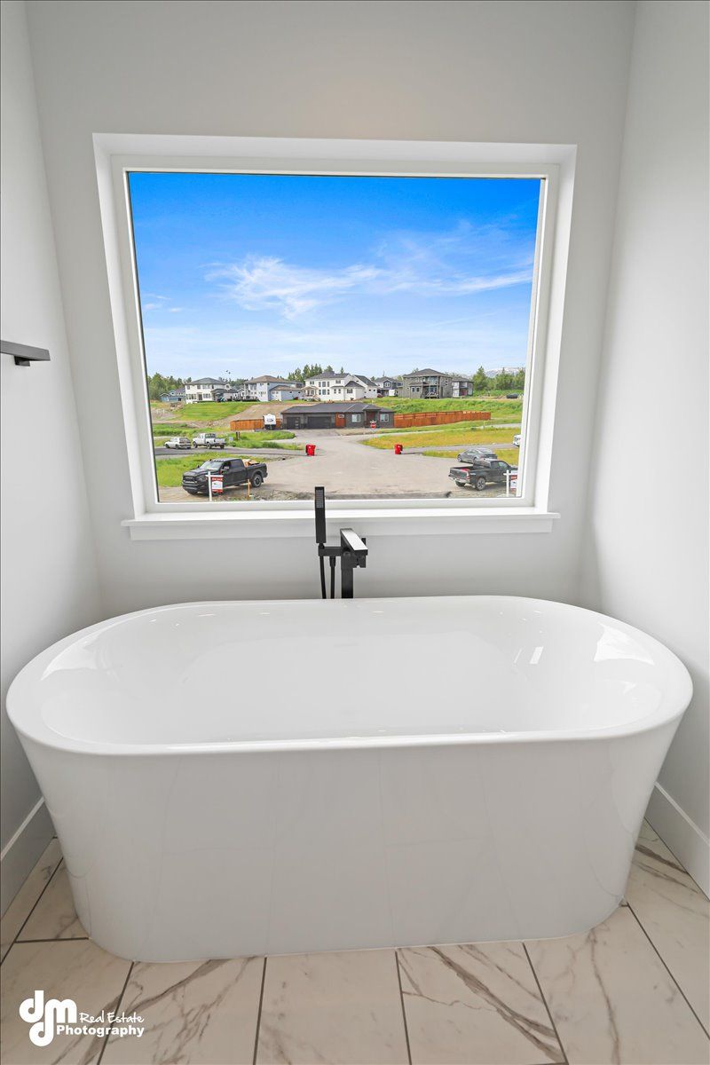 Freestanding white bathtub beneath a large window with a view of a landscaped neighborhood.