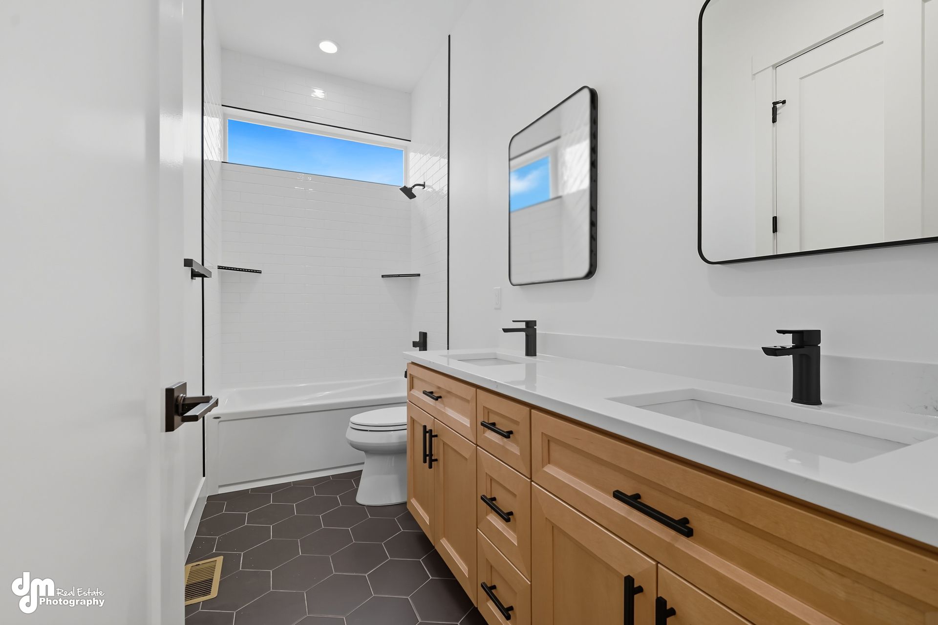 Bright bathroom with wooden vanity, black fixtures, large mirror, and shower with blue sky window.