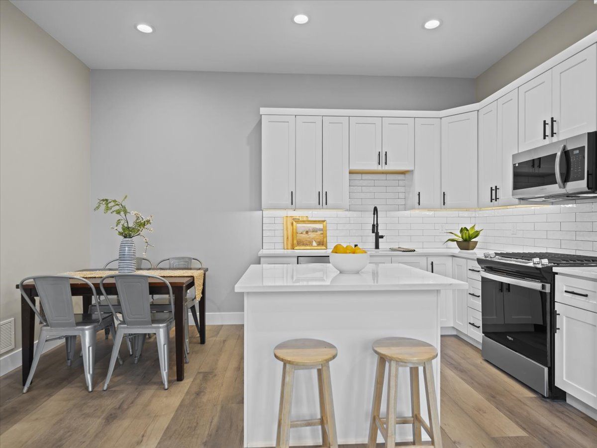 Modern white kitchen with island, two stools, dining table, and stainless steel appliances