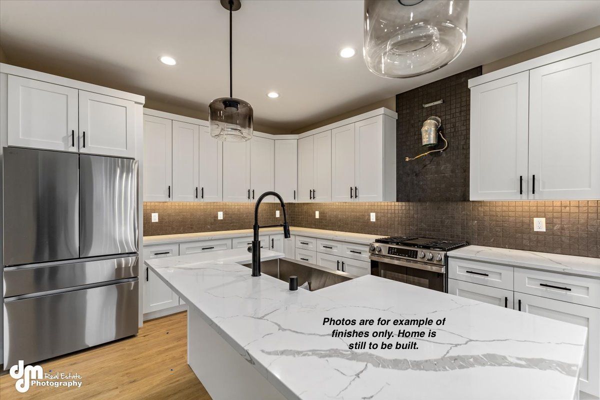Modern white kitchen with stainless steel fridge, marble island, black pendant lights, and wood floors