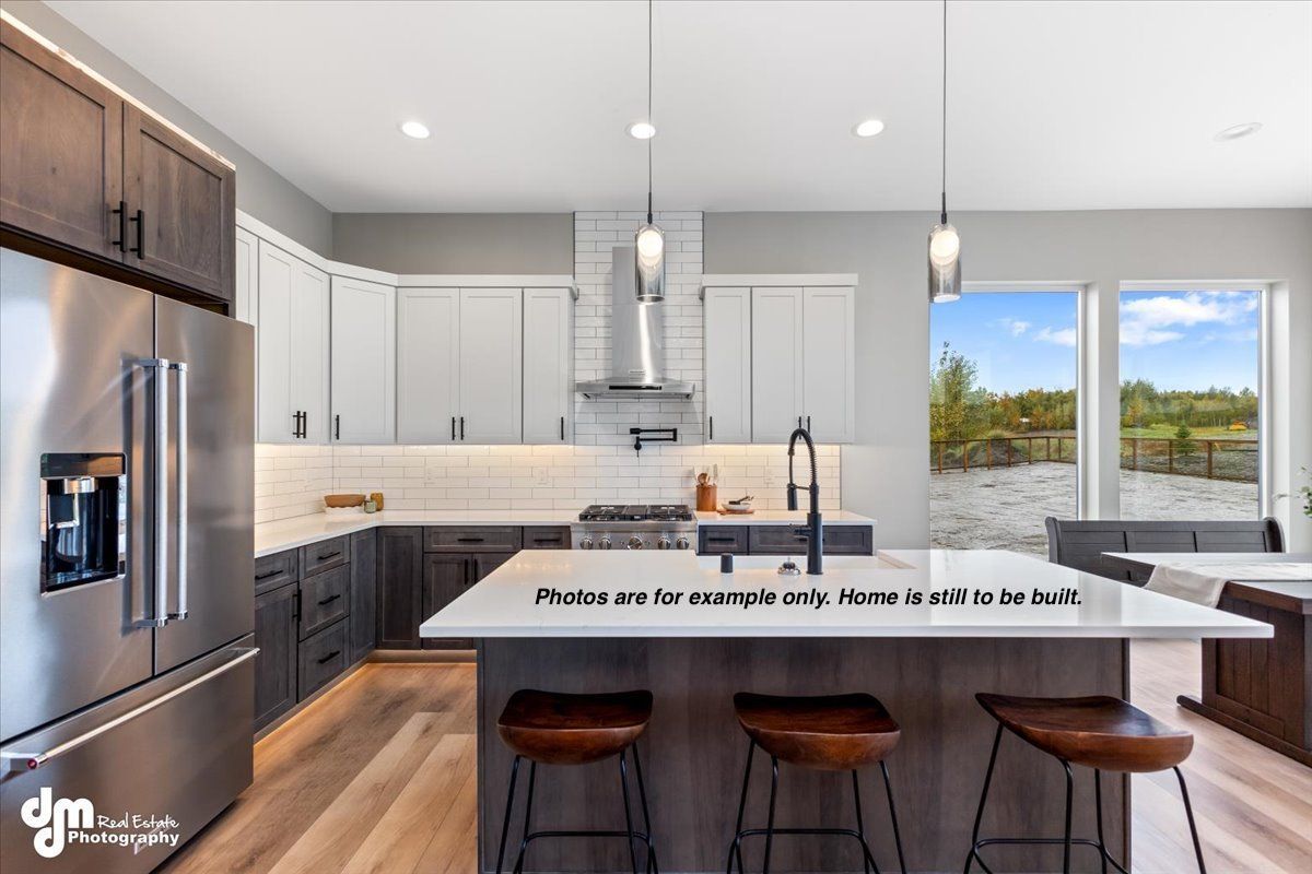 Modern kitchen with white island, stainless fridge, pendant lights, and large windows overlooking greenery