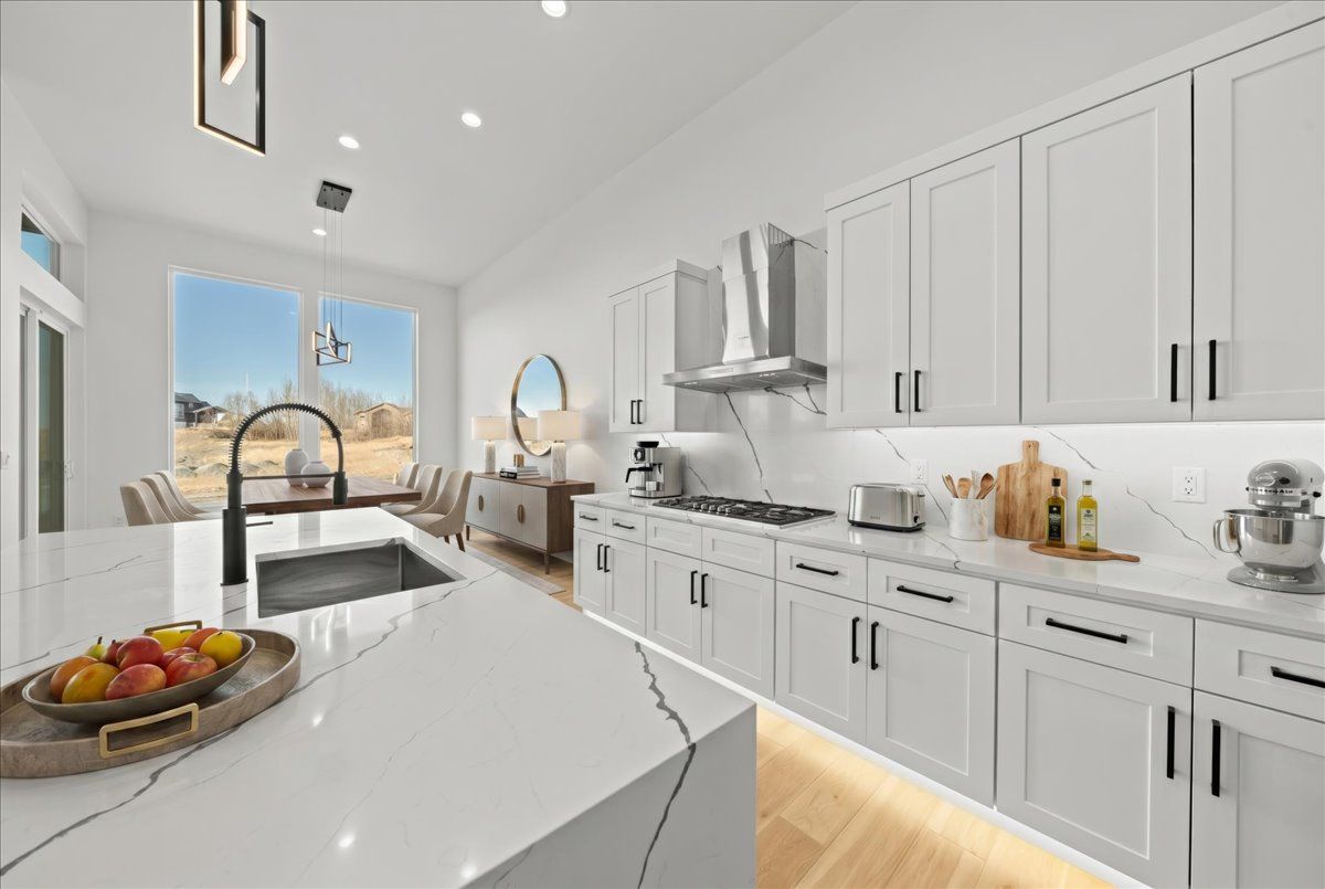 Bright modern white kitchen with island, sink, and a dining area by large windows overlooking a city view