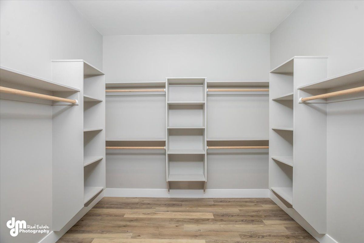 Walk-in closet with white shelving, hanging rods, and wood flooring