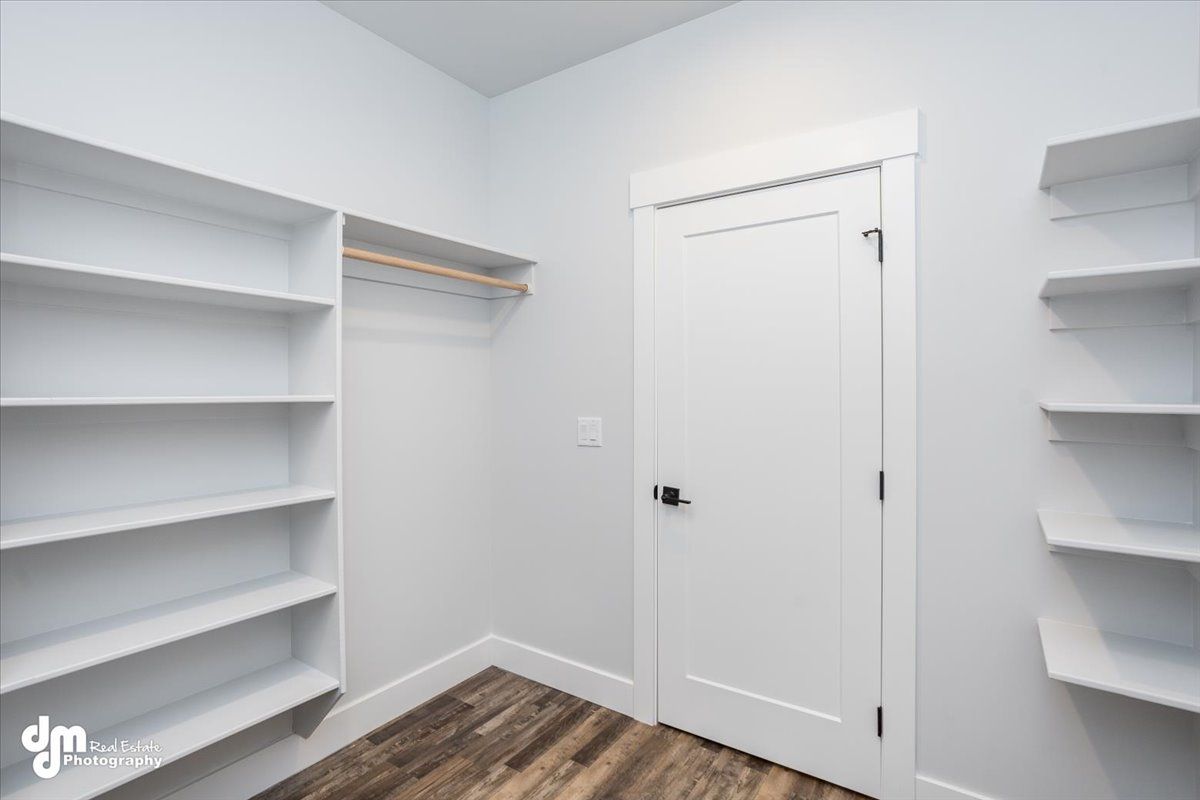 Empty white walk-in closet with built-in shelves, hanging rods, and a closed door.