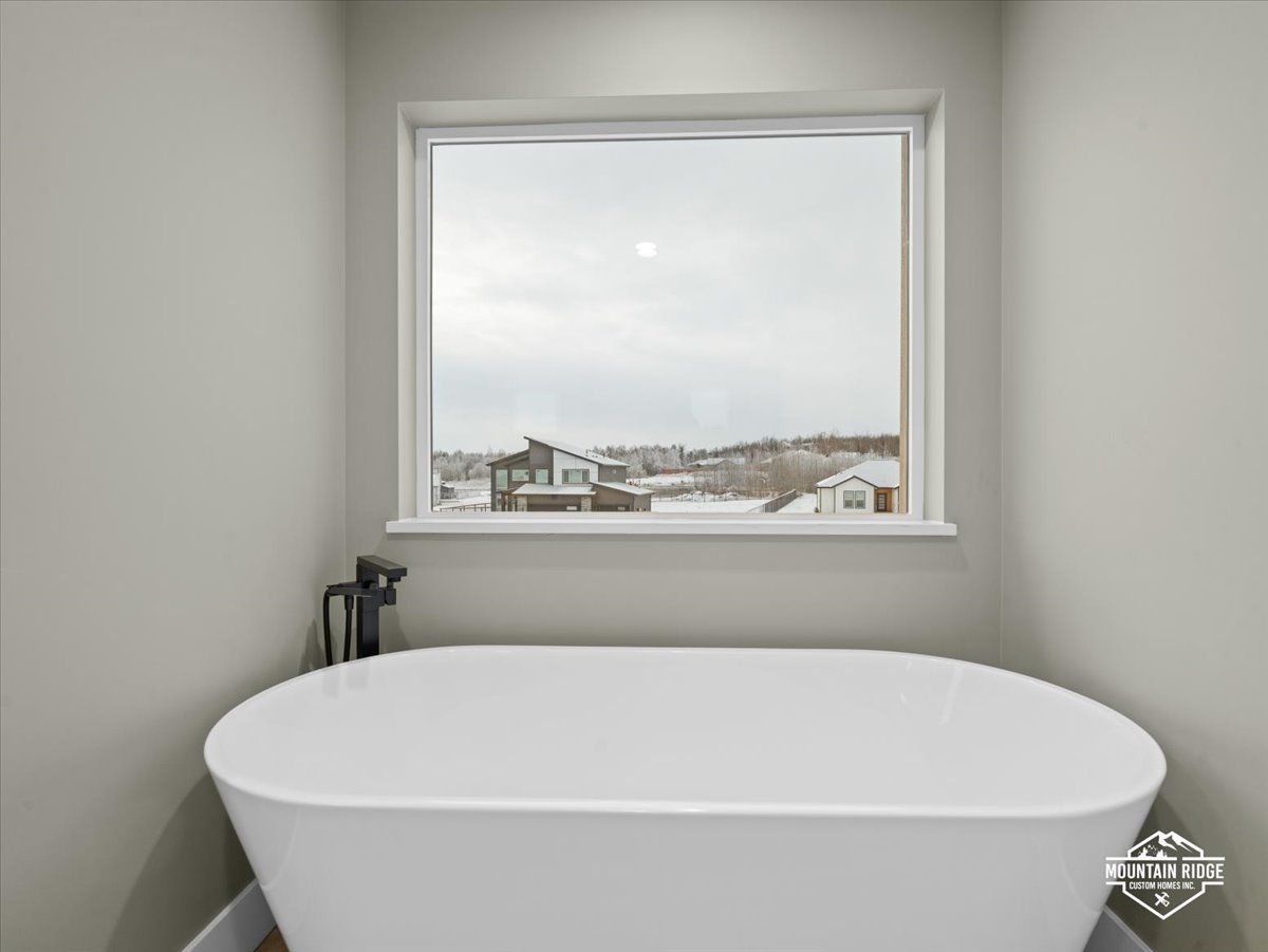 Modern bathroom with a white tub beneath a window overlooking a snowy cityscape