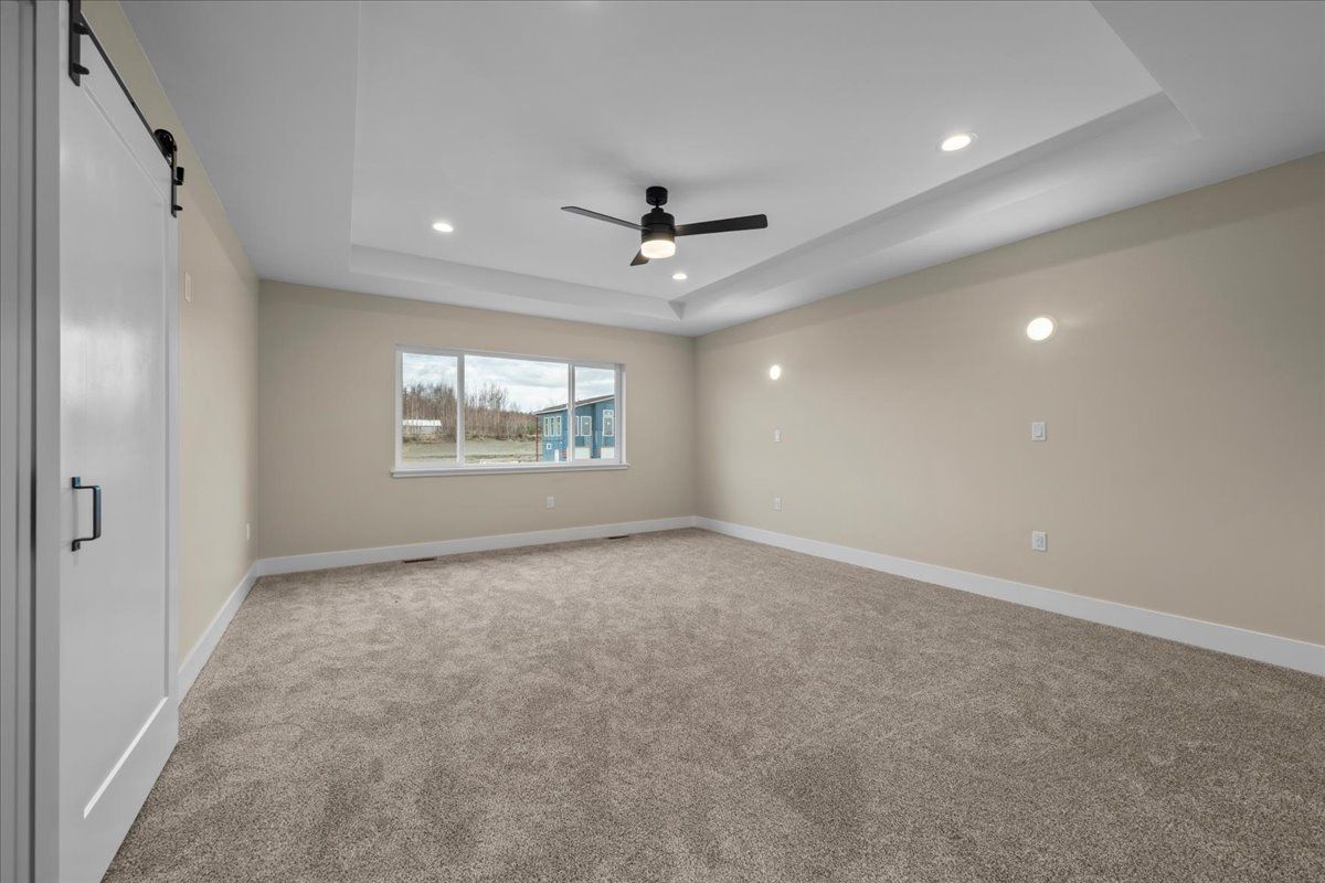 Empty beige bedroom with carpet, tray ceiling, ceiling fan, and a window