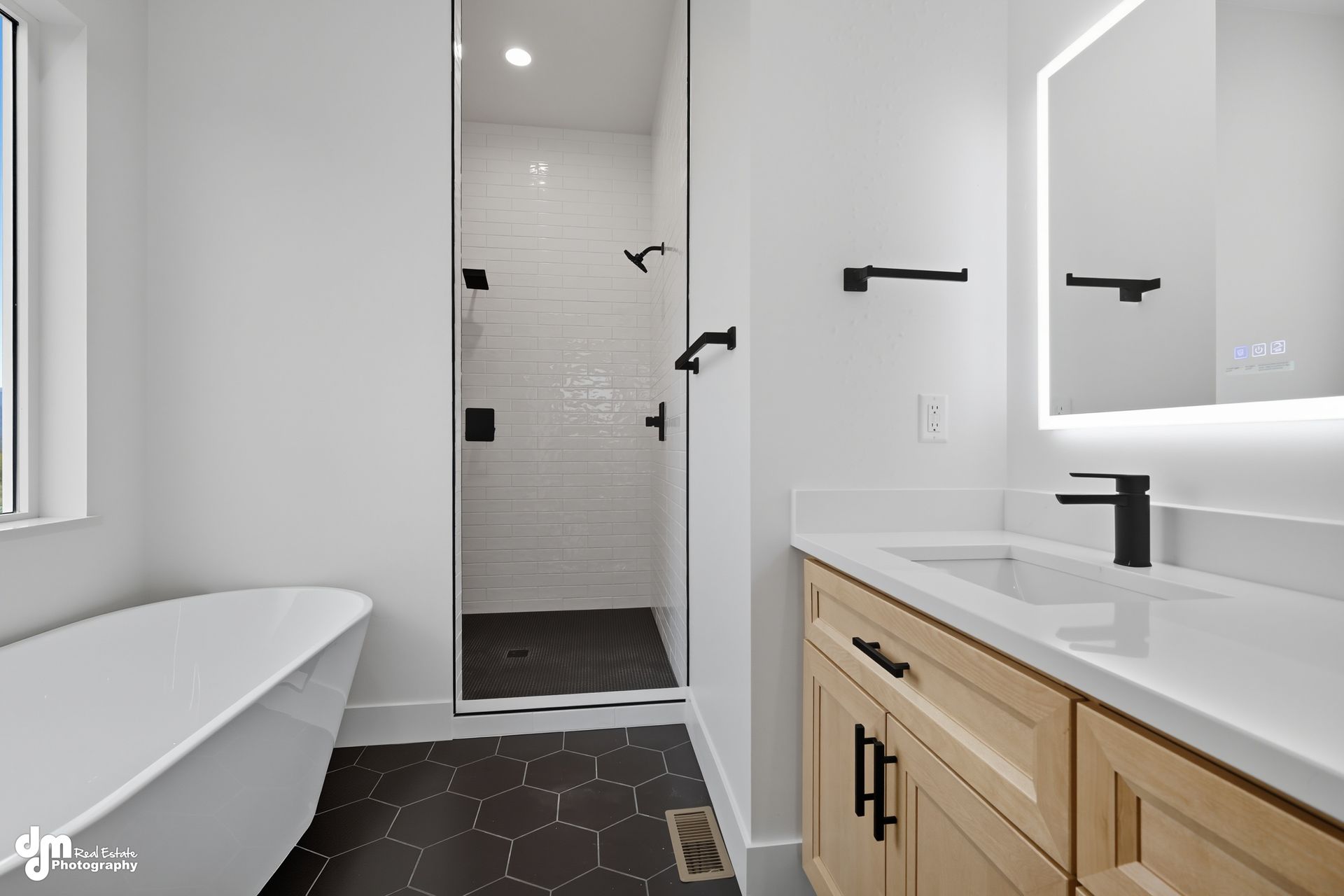 Modern bathroom with freestanding tub, double vanity, black fixtures, and tiled shower corridor