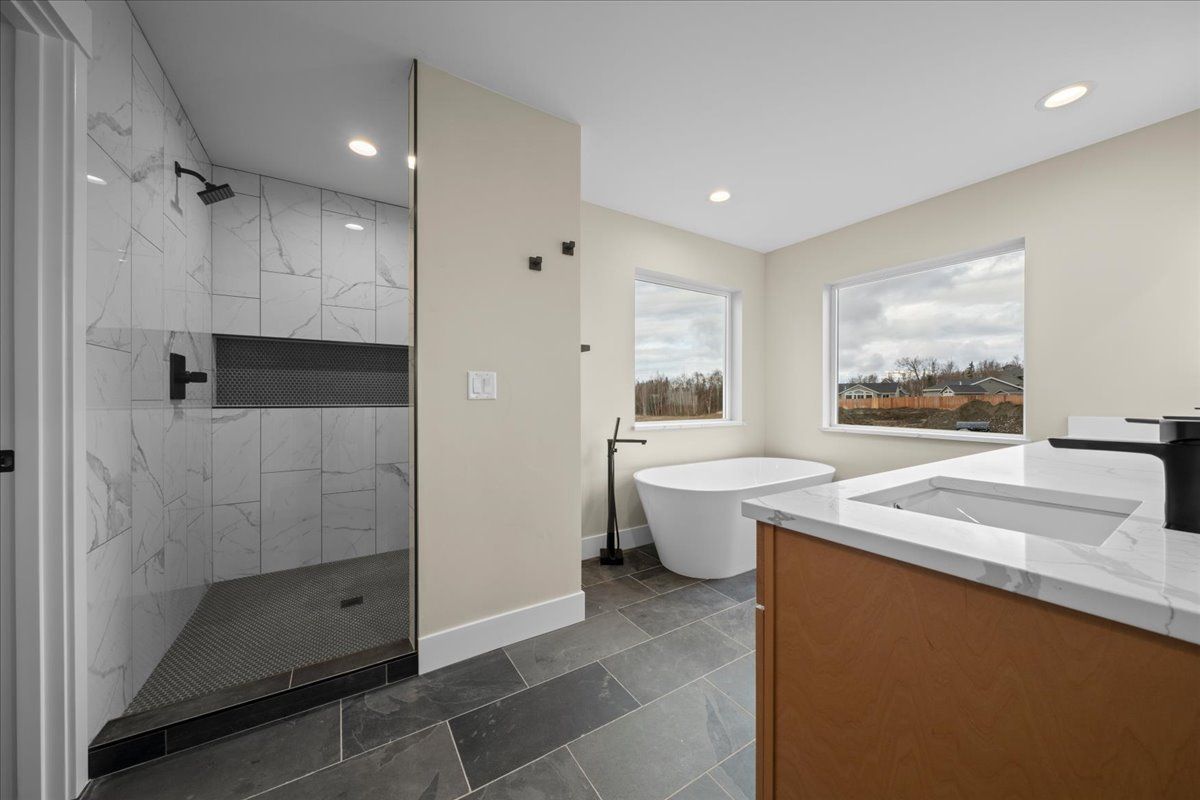 Modern bathroom with walk-in shower, freestanding tub, vanity, and large windows looking outside