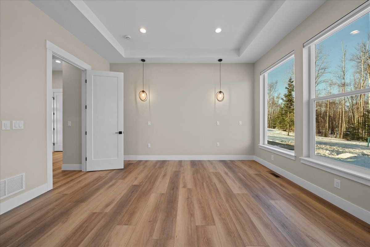 Empty modern room with wood floors, beige walls, recessed lights, and large windows overlooking snow outside