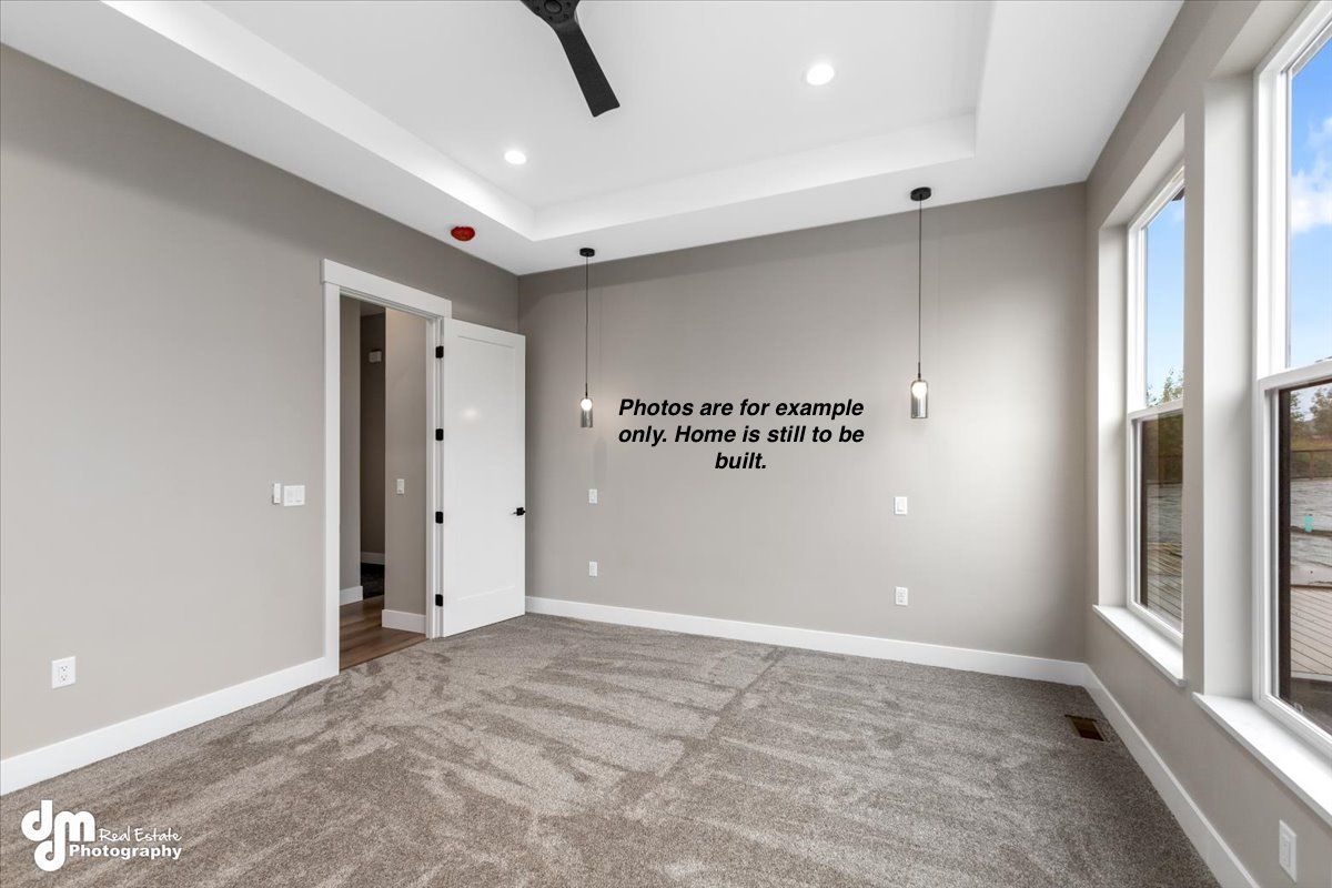 Empty gray carpeted room with large windows and recessed ceiling lights, listing text on the wall.