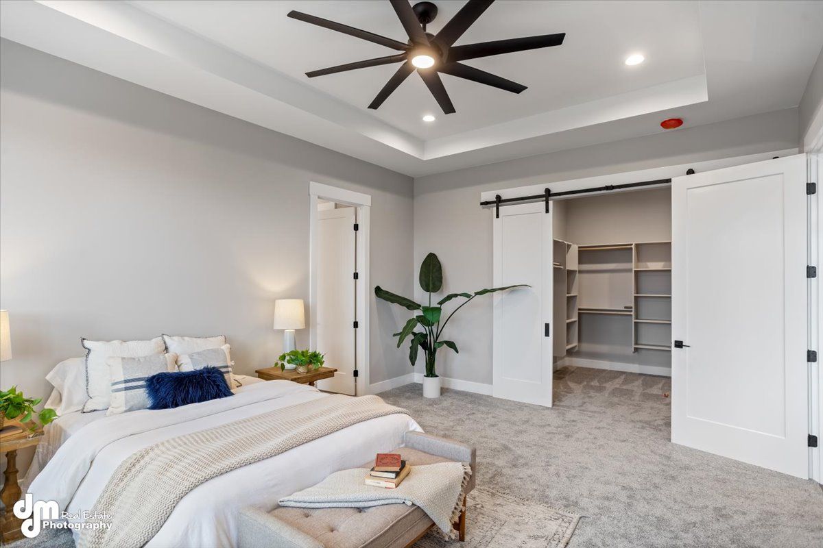 Bright bedroom with white walls, black ceiling fan, bed, nightstand, plant, and open closet shelves