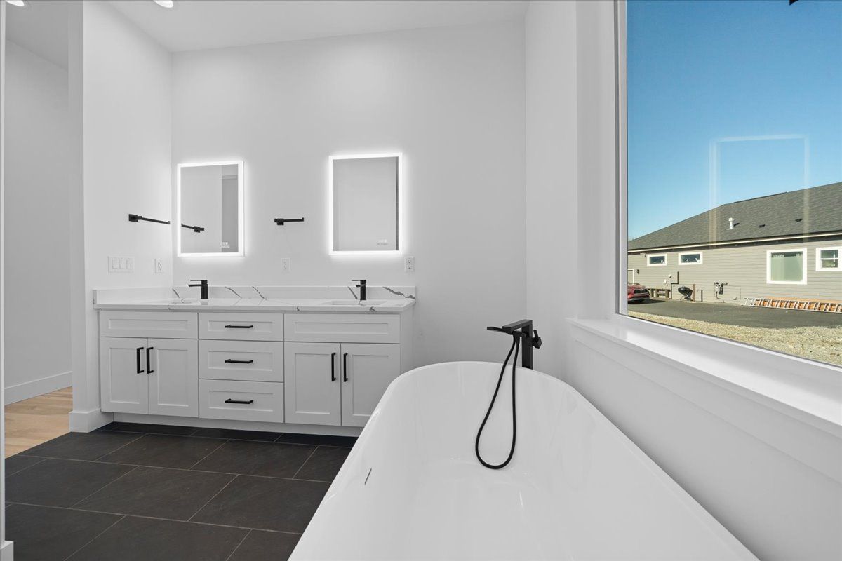 Bright bathroom with double vanity, mirrors, and a freestanding tub by a window.