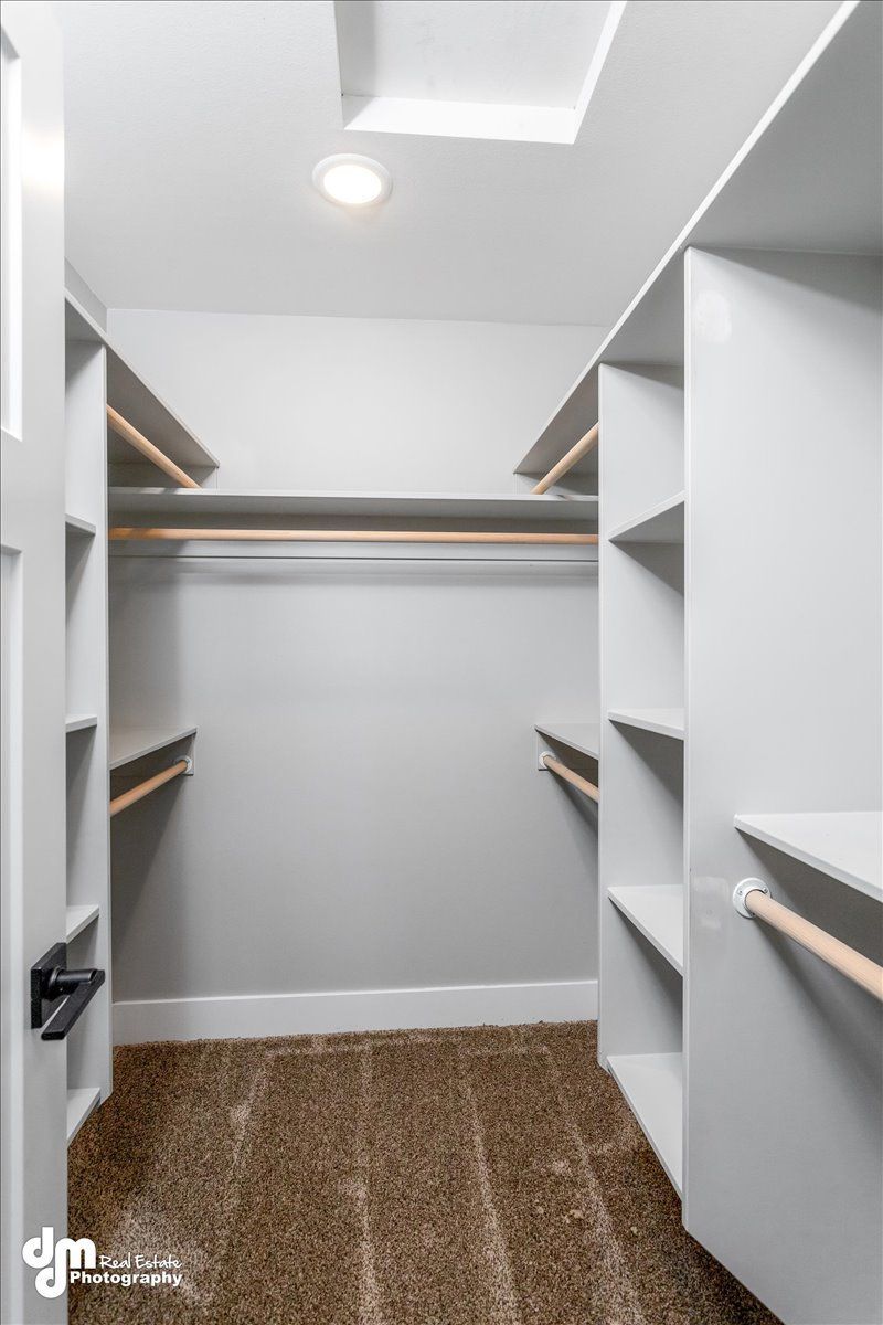 Walk-in closet with white shelves, hanging rods, and brown carpet under a ceiling light