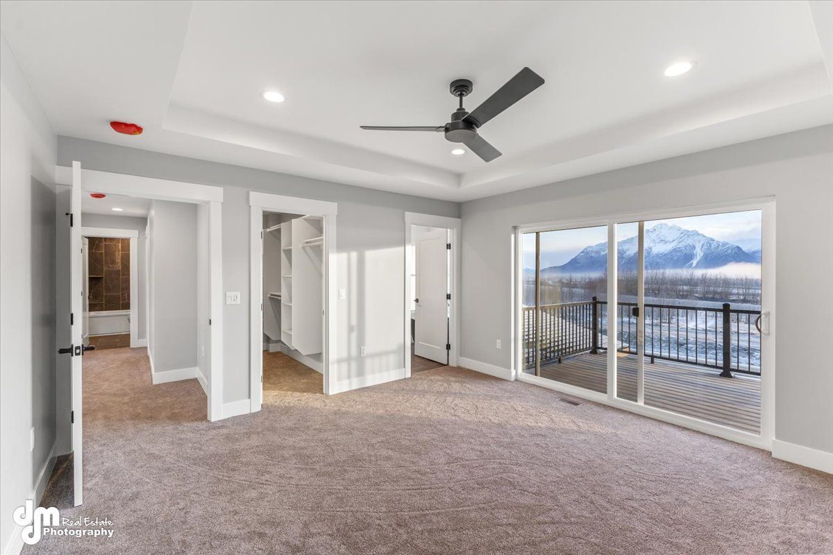 Empty carpeted bedroom with ceiling fan, white walls, and sliding glass doors to a snowy mountain view