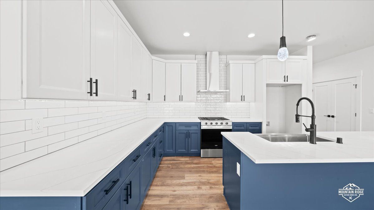 Modern white kitchen with navy cabinets, wood floor, and a large island sink