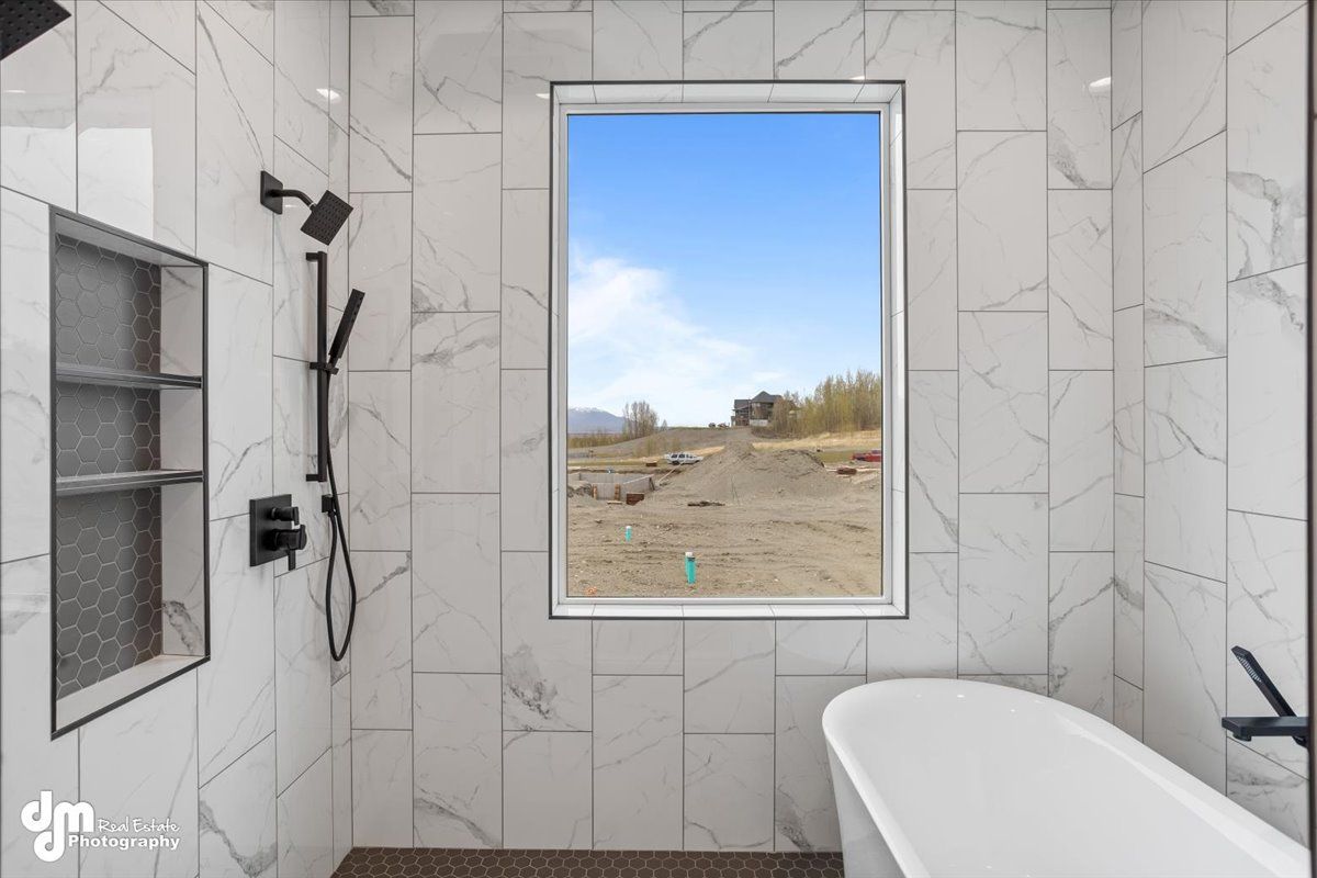 Modern bathroom with marble tile, walk-in shower, freestanding tub, and a large window overlooking a field