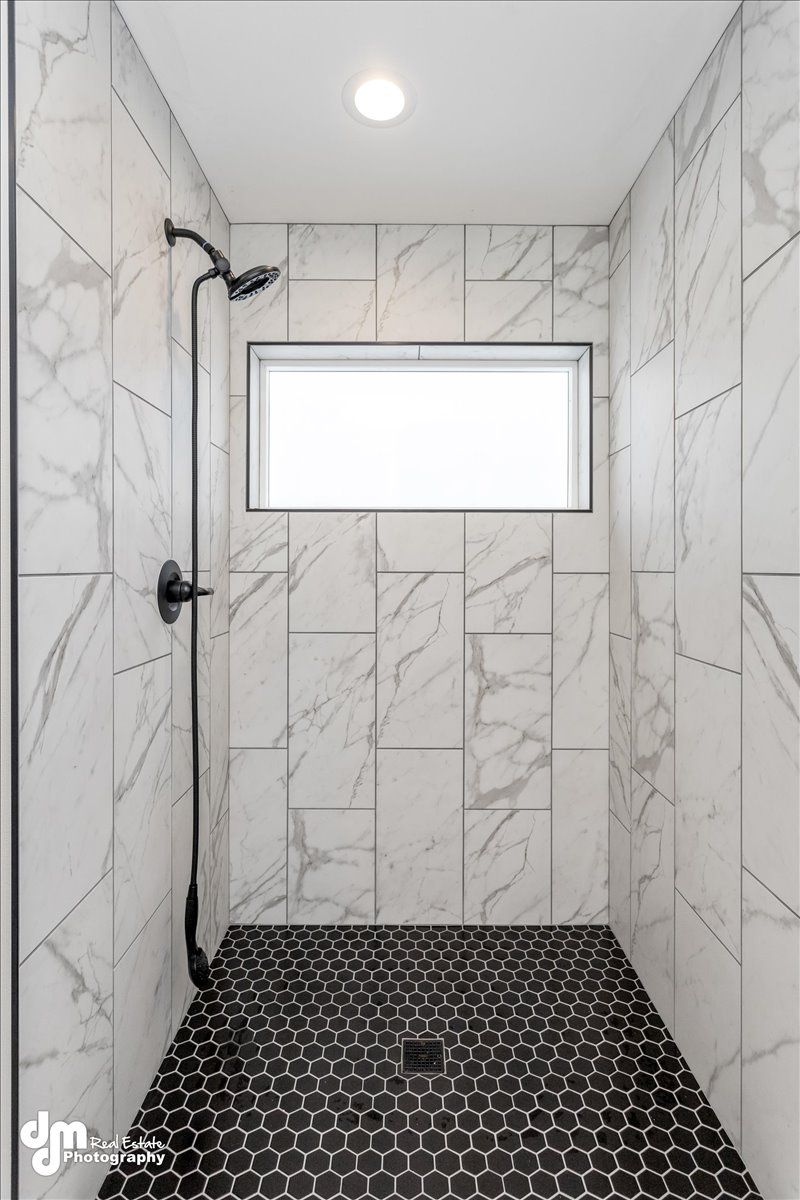 Modern tiled walk-in shower with black fixtures, a small frosted window, and dark pebble floor.